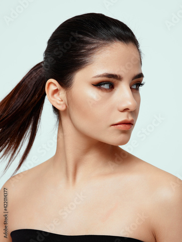 brunette in a black dress with bare shoulders looking to the side on a light background