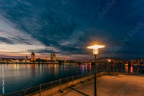 View of Cologne Cathedral with Hohenzollern Bridge at nightfall and a lamppost in the foreground, Germany. © Bernhard