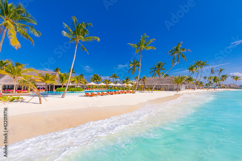 Luxurious beach resort with swimming pool and beach chairs or loungers under umbrellas with palm trees and blue sky. Summer island travel and vacation destination. Relax lifestyle, leisure carefree