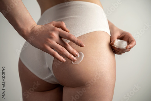 Body care. Woman applying cream on legs and buttocks. girl in a black thong, athletic. studio shot on a blue background