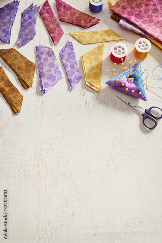 Fototapeta Naklejka Na Ścianę i Meble -  Stacks of multi-colored pieces of fabric, scissors, pincushion, spools of thread on a white surface