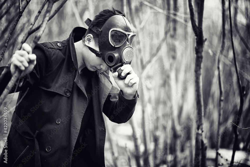 Foto Stock The guy in the coat and gas mask. Post-apocalyptic portrait of  Asian masked from radiation. The boy is Korean in a mask from poisoning  with gases. Post-nuclear mask on the