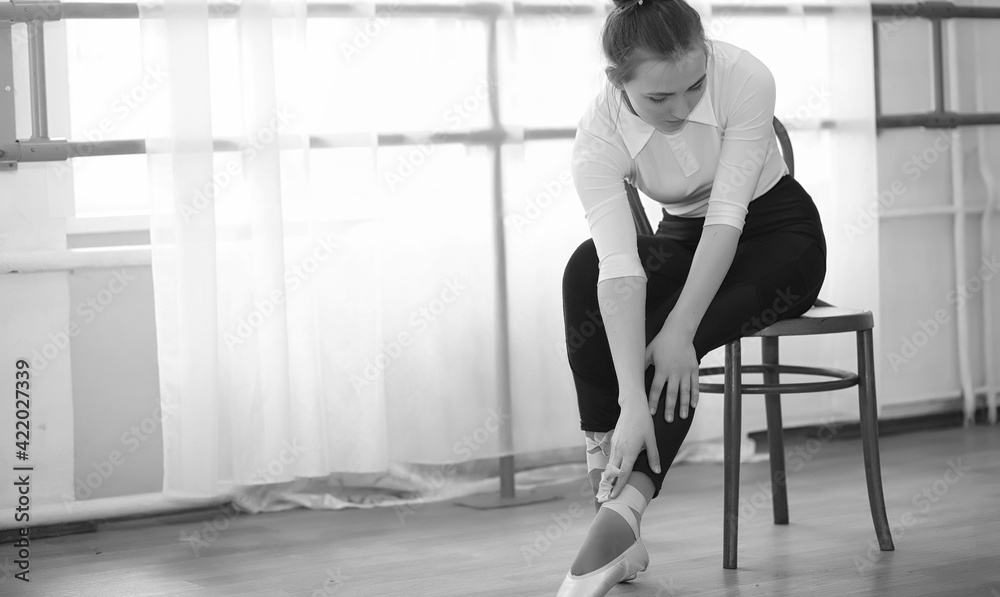 Obraz premium Young ballet dancer on a warm-up. The ballerina is preparing to perform in the studio. A girl in ballet clothes and shoes kneads by the handrails.