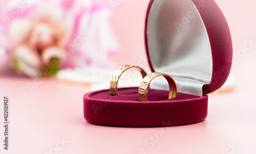 a pair of gold rings in a special case of red color on a background of flowers © Dinara