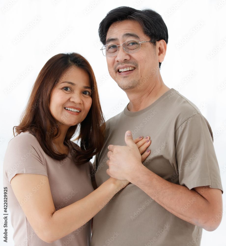 Half-body horizontal portrait shot of cute smiling senior Asian lover couple standing at home. Husband and wife holding hands together, touching at man heart and looking at each other eyes. Half-body horizontal portrait shot of cute smiling senior Asian lover couple standing at home. Husband and wife holding hands together, touching at man heart and looking at each other eyes.