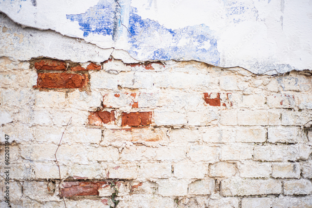 Old wall surface with crumbling plaster. Old brick wall for background. Red bricks and cement pavement. The dilapidated facade of the house with damaged plaster.