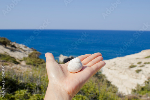 A girl holds a seashell in her hands against the background of the Mediterranean sea, Crete island, Greece.