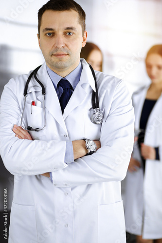 Professional doctor with a stethoscope is standing with crossed arms in a sunny clinic. Perfect medical service in hospital. Best medicine concept