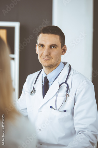 Friendly male doctor and patient woman discussing current health examination while sitting in clinic. Perfect medical service in hospital. Medicine and healthcare concept