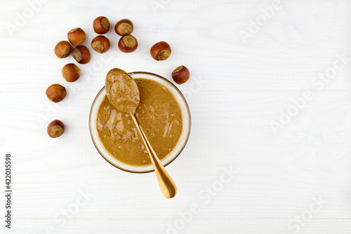 Natural organic raw hazelnut paste in a glass bowl and hazelnuts on a white wooden background. Diet natural breakfast. Top view.
