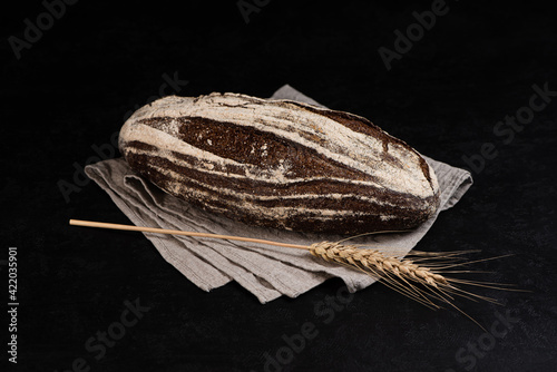 Obraz na płótnie Artisan sourdough rye bread on dark background. Whole loaf of bread on textile napkin and rye spikelet. w salonie