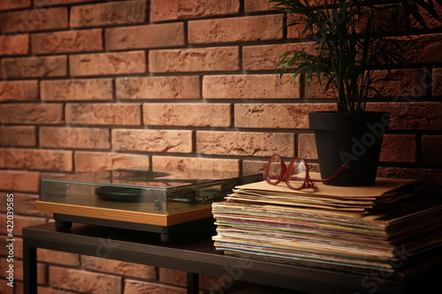 Stylish turntable and vinyl records on shelving unit near red brick wall