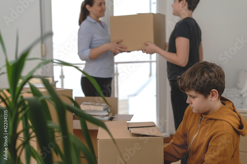 
A sad boy packs his things to move out into a new apartment while other family mambers talk in the background