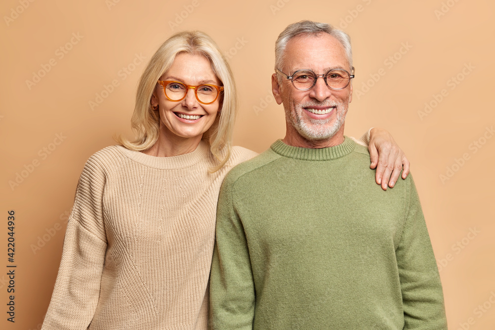 Φωτογραφία Smiling mature couple embrace look gladfully at camera pose for family portrait happy children came to visit them wear transparent glasses casual jumpers isolated over brown background