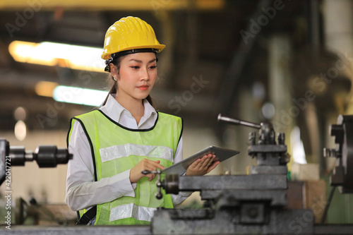 Asian woman engineering manager in safety hard hat and reflective cloth is inspecting inside the lathe factory using digital tablet with copy space