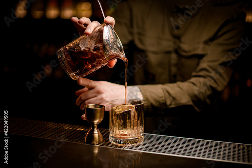 bartender s hand holds mixing cup with cold cocktail and pours it into old-fashioned glass