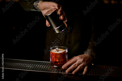 view of cocktail glass on bar which man bartender decorates with powdered sugar
