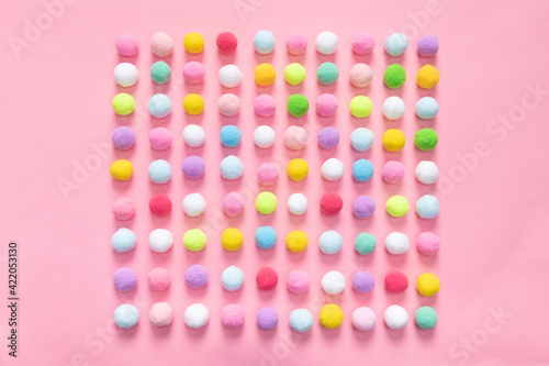 Top view of colorful pom pom balls forming a square shape on pink background