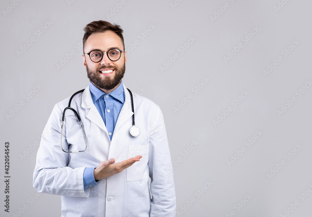 Cheerful male doctor in uniform pointing at empty space over grey studio background, panorama Cheerful male doctor in uniform pointing at empty space over grey studio background, panorama