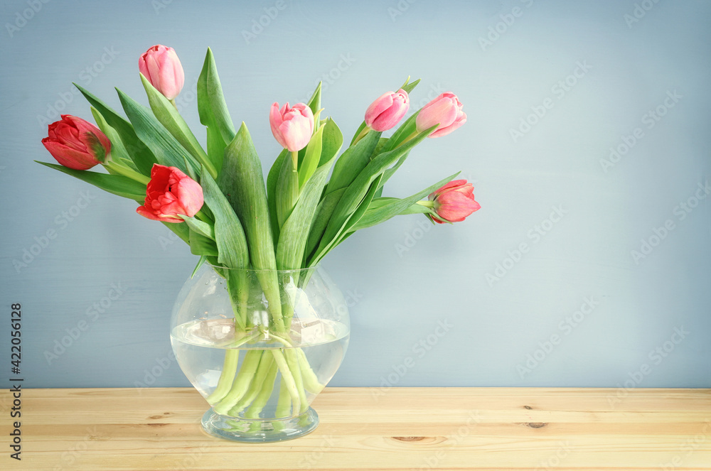 spring bouquet of red and pink tulips flowers in the glass vase over wooden table