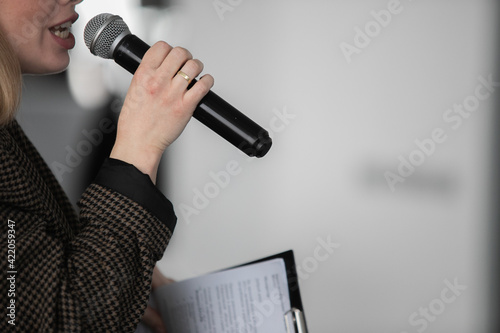 Presenter Giving Presentation and Moving Hand Holding Projector Remote Control. Corporate Business Marketing Manager and Sales Pitch. Speaker in Business Meeting Room Holding Microphone Next to Screen photo