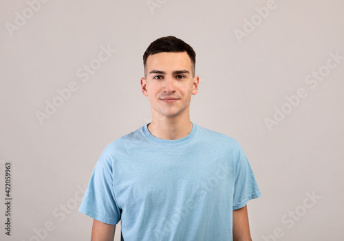 Wallpaper Mural Portrait of positive young guy in t-shirt looking at camera on light grey studio background Torontodigital.ca
