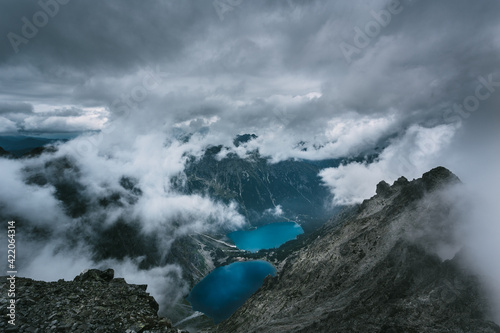 View of two lakes of glacial origin  with a clear blue water surface  mirroring the sky   between the rocky mountains. The sky is cloudy  full of clouds passing between the tops of the mountains.