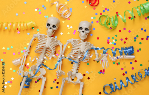 Skeletons with colored streamer and confetti on yellow background. Halloween celebration  fun and fear. Top view. Flat lay