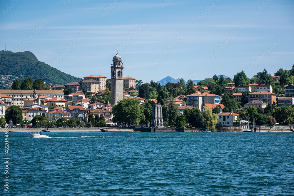 a picturesque town on the shores of Lake Maggiore in Italy. The coastal buildings are crowned with a high bell tower of a Catholic church