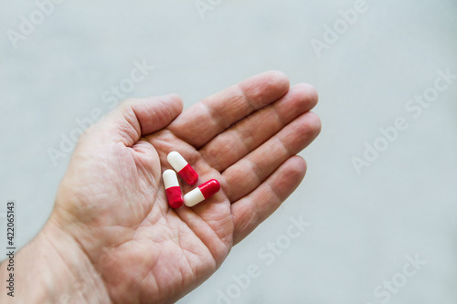 Several red and white pills on the palm of a human hand on a gray background. Medicine. Pharmaceuticals. Bioactive additives. Vitamins. Illness. Disease. Medical capsules for health.