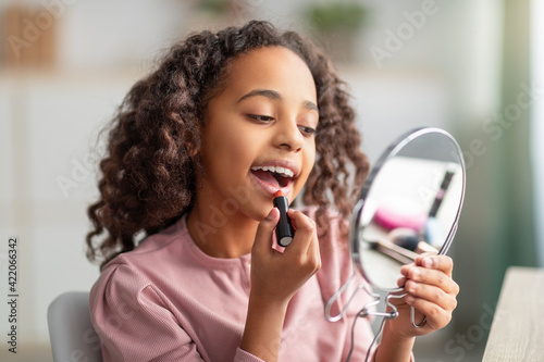 Daily make up. Happy teenage lady applying lipstick  holding mirror and looking at herself