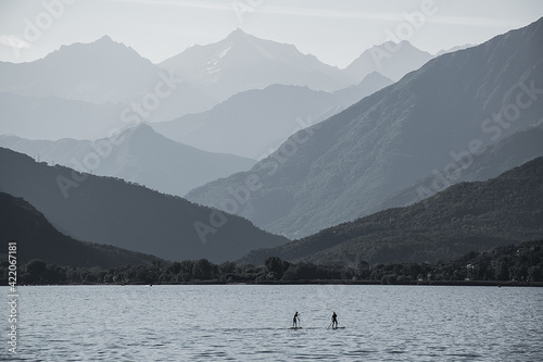 Tourists on SUP in the middle of the vast expanses of Lake Maggiore in Italy against the backdrop of beautiful mountains. The contour lighting creates a halftone perspective.