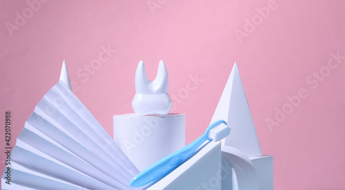 Dental care concept. Tooth and toothbrush on a showcase with geometric shapes. Pink background