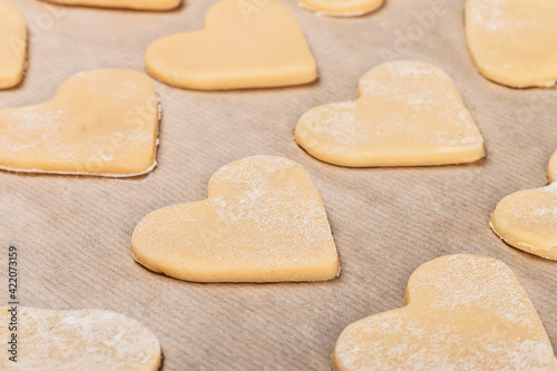 Homemade shortbread cookies in the shape of a heart are neatly laid out on parchment in flour. Close-up, top and side view.