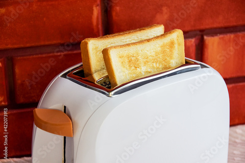 A close-up of two toasted toast breads. Two toasts on a background of a red brick wall. Fried toast popping out of a toaster against a brick wall. The toast pops up, pops out of the toaster.