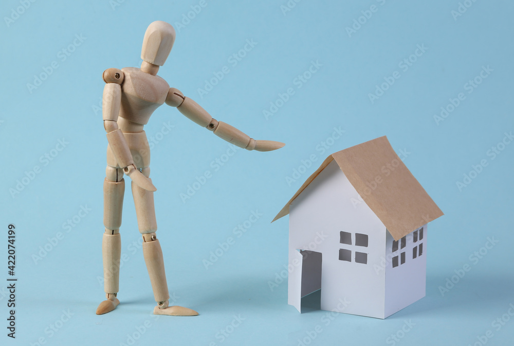 Home sale concept. Puppet realtor points to a house figurine on a blue background Home sale concept. Puppet realtor points to a house figurine on a blue background