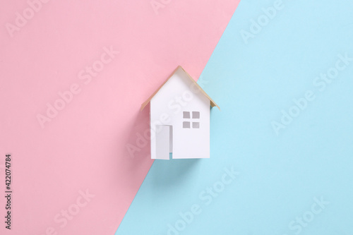 Mini paper house figurine on pink blue background. Flat lay