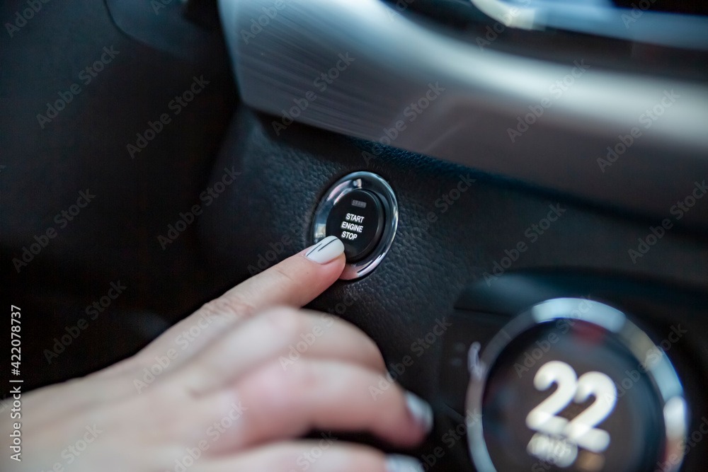 hand finger presses the start stop button in a modern car. close-up. no face. selective focus