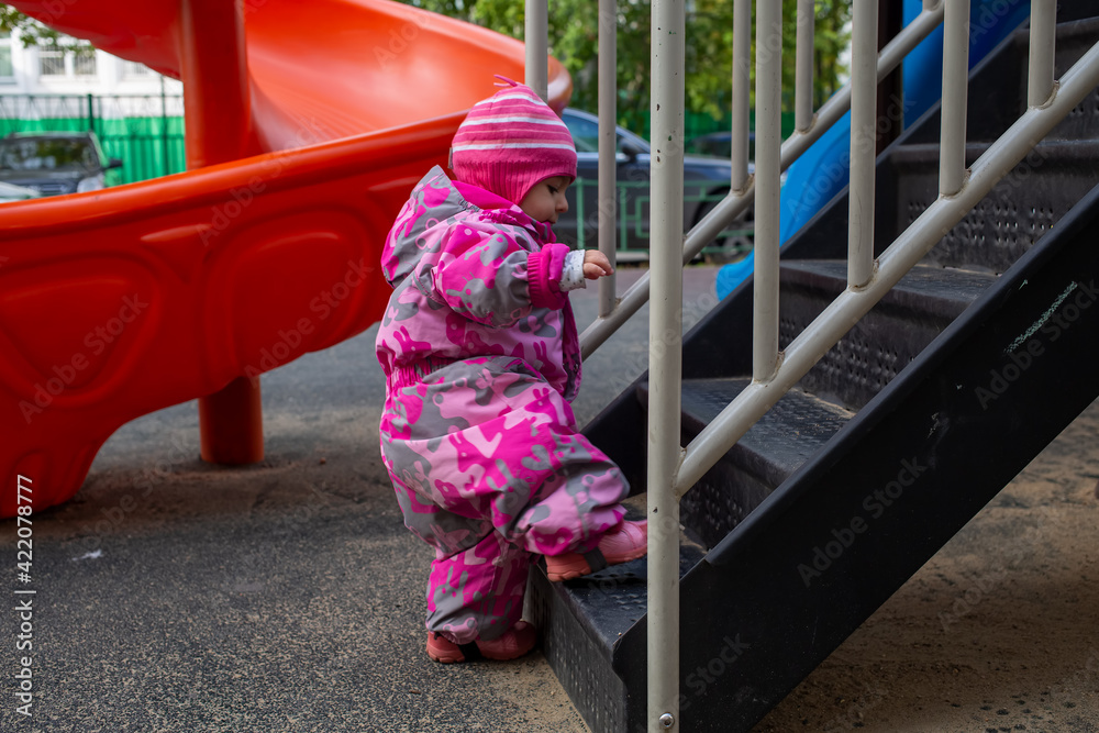 adorable toddler climbs the stairs on the playground. toddler baby dressed in a snowsuit. autumn or winter, cold season