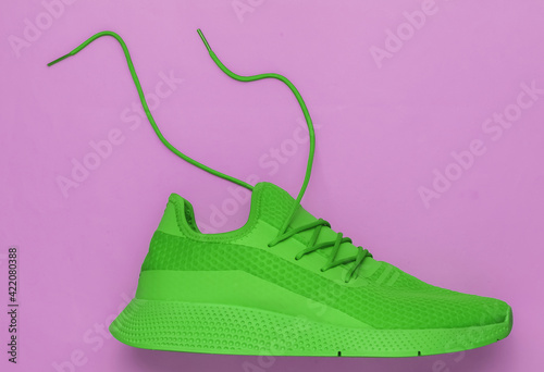 Green sport running shoe with untied laces on pink background. Top view