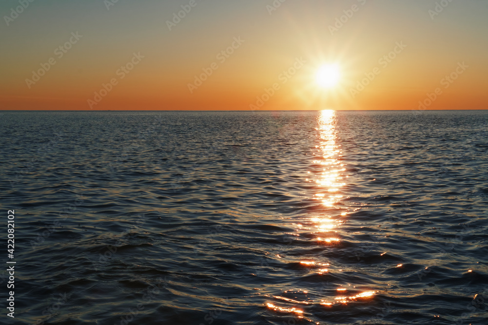 Fototapeta premium A sunny sunset on the sea stretching into the horizon with a path and highlights on the sea.