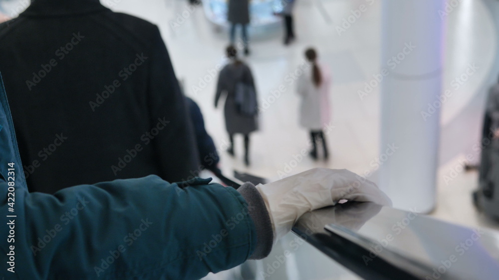 Arm wearing winter jacket and white protective glove grabs escalator black handrail in shopping mall close view slow motion Arm wearing winter jacket and white protective glove grabs escalator black handrail in shopping mall close view slow motion