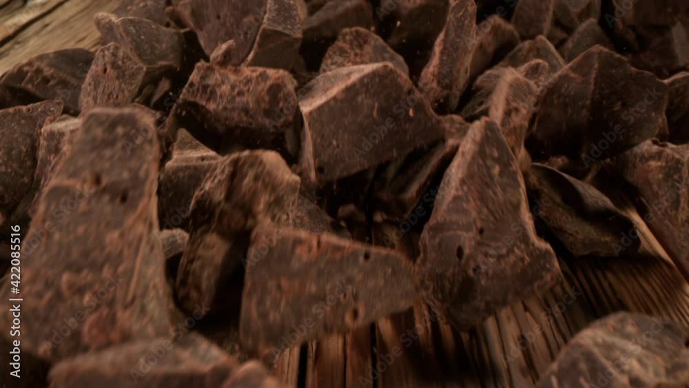 Super Slow Motion Detail Shot of Chocolate Chunks Rolling Towards on Wooden Background at 1000fps with Camera Motion.
