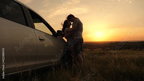 Happy enamored travelers man and woman stand next to car and admire beautiful sunset at campsite. Tourists travel by car, hug, admire sunrise, nature. Free travelers, tourists. Family travel by car. © zoteva87
