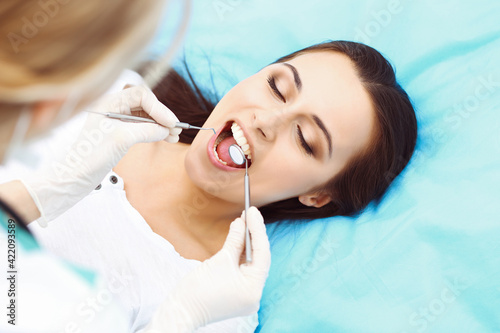 Young female patient visiting dentist office.Beautiful woman with healthy straight white teeth sitting at dental chair with open mouth during oral checkup while doctor working at teeth