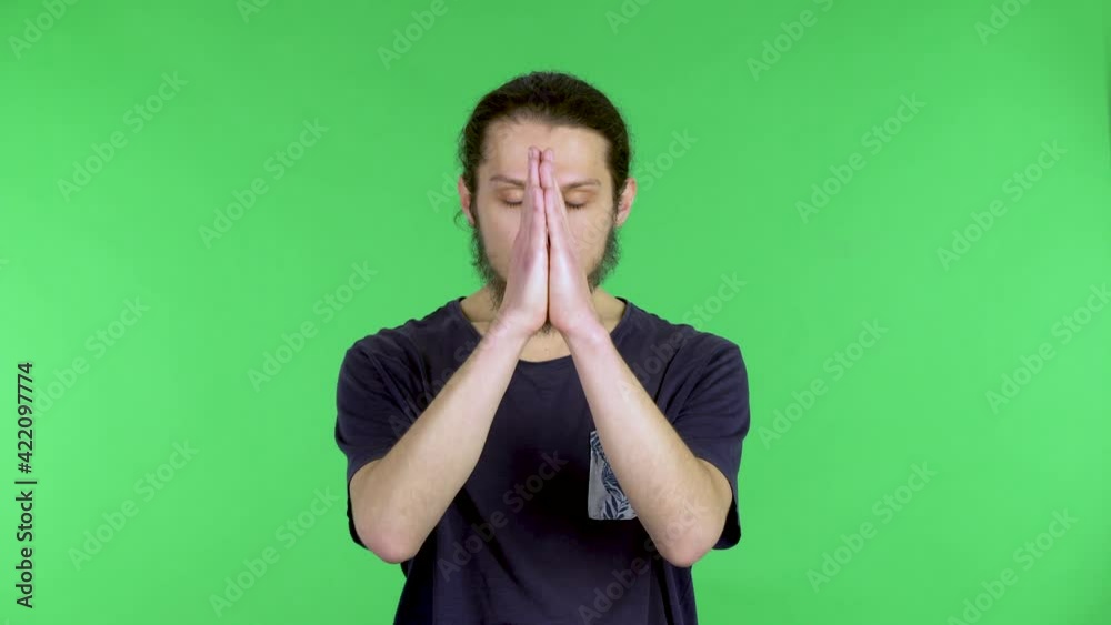 A darkhaired young man in a black Tshirt holds his palms together in a prayer gesture. A man in the studio on a green screen. Close up. A darkhaired young man in a black Tshirt holds his palms together in a prayer gesture. A man in the studio on a green screen. Close up.