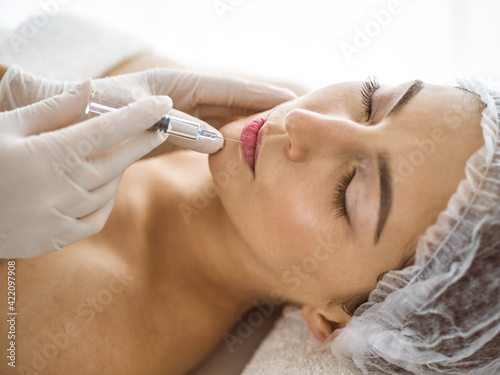 Beautician doing beauty procedure with syringe to face of young brunette woman in sunny clinic. Cosmetic medicine and surgery  beauty injections