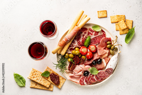 Appetizers with differents antipasti, charcuterie, snacks and red wine on white background. Sausage, ham, tapas, olives and crackers for buffet party. Top view, flat lay photo