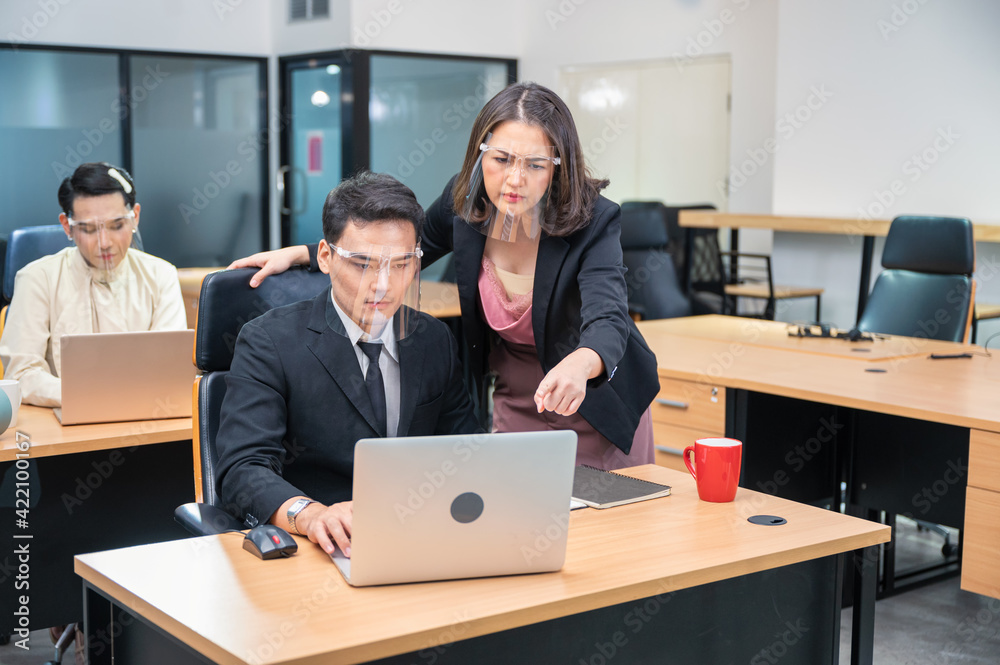 Serious asian female executive consulting with male colleague working with laptop at desk in modern office Serious asian female executive consulting with male colleague working with laptop at desk in modern office
