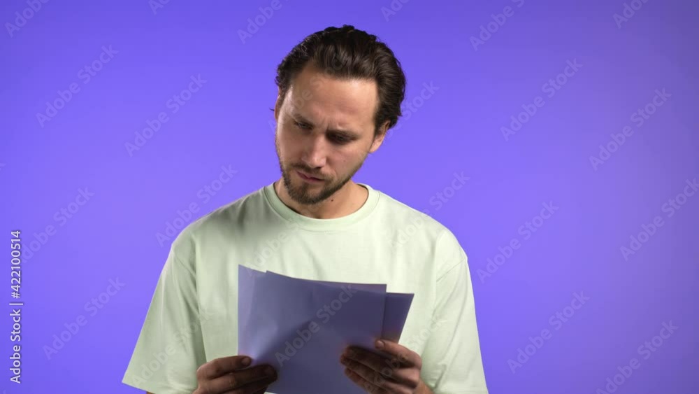 Young handsome man checks documents, utility bills, report. Guy isolated on violet background. He is satisfied Young handsome man checks documents, utility bills, report. Guy isolated on violet background. He is satisfied